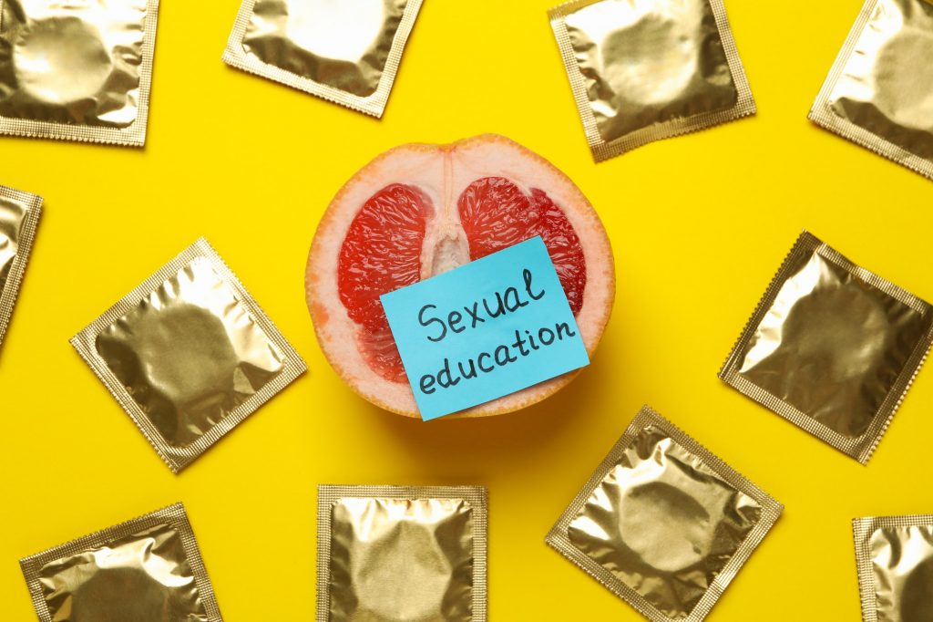 Pomelo with text Sexual education and condoms on yellow background
